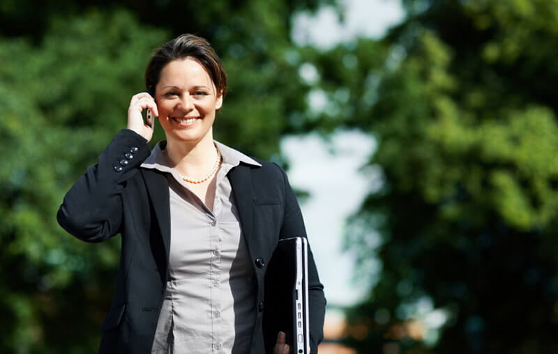 Portrait of a business woman holding a laptop and speaking on the cellphone outdoors